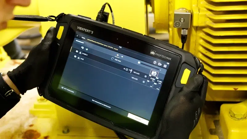 Worker holding VIBXPERT III Balancer tool measuring vibration from motor that's painted yellow